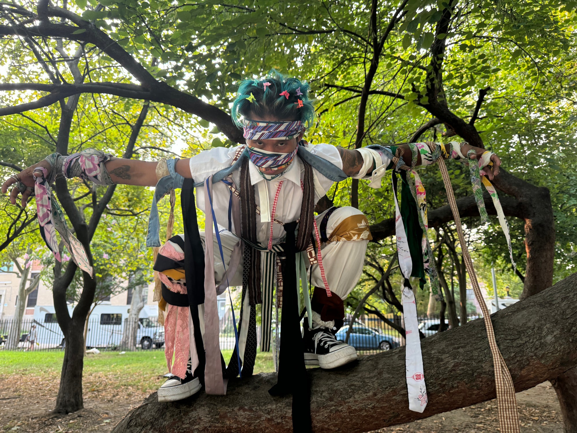 man posing in tree with many neck ties and belts wrapped around