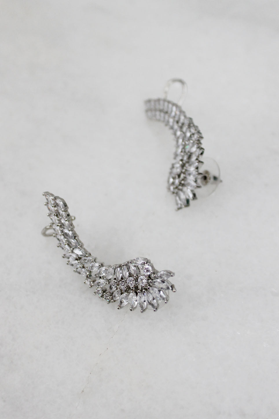 detail view of christian siriano angel wing ear climbers. features post with a push back closure and a hook at the top to loop around the ear. marquis cut and round cut cubic zirconia