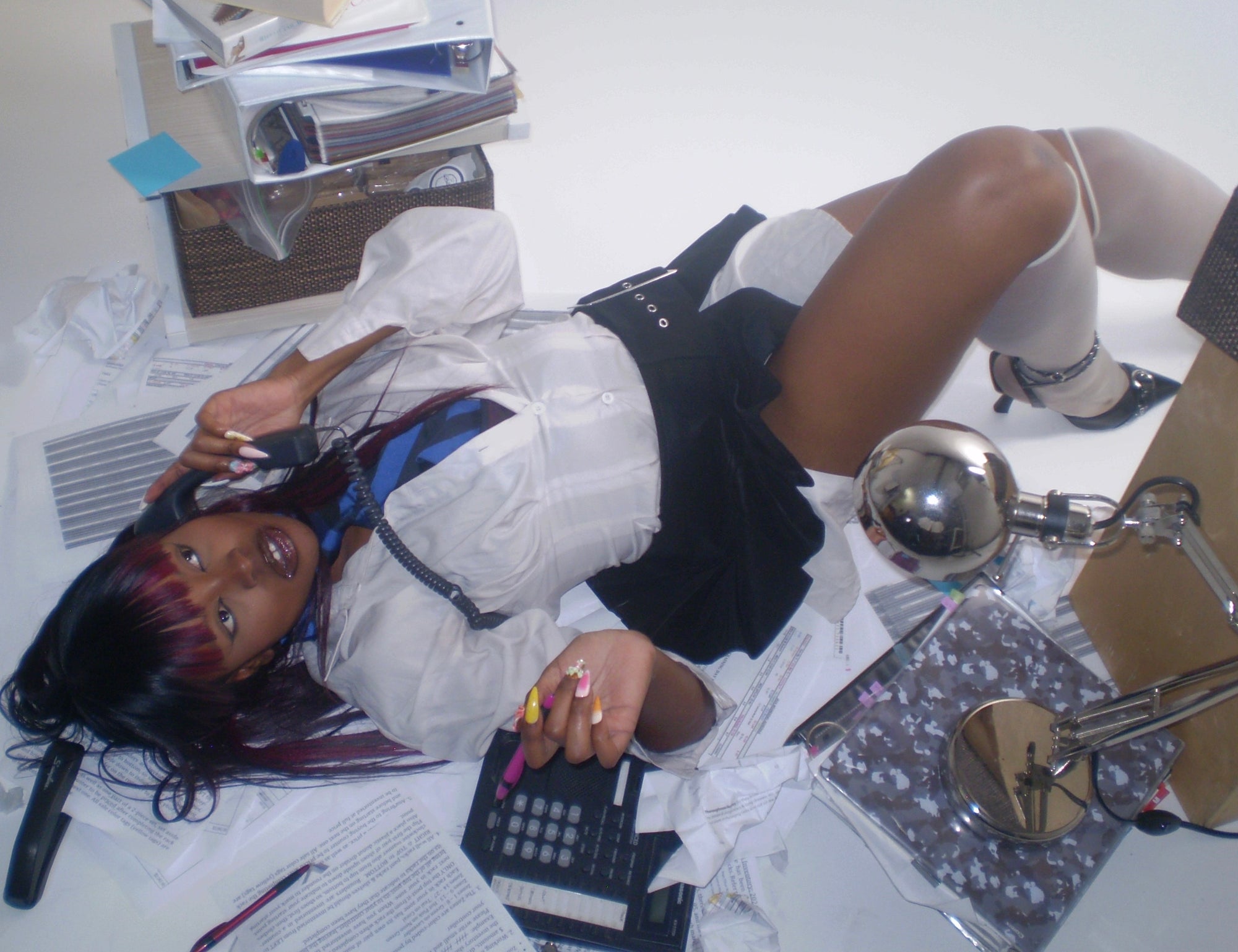 editorial image of 'office siren' ascetic model laying on floor amongst office supplies on phone 