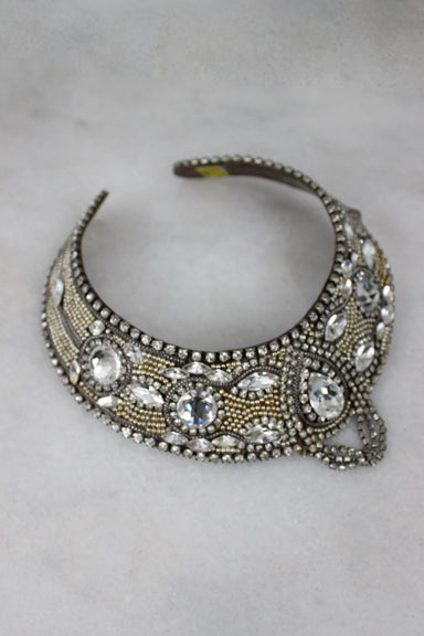  unlabeled neck ring. features multiple rhinestones with marquise and round cuts. smaller gold and silver beads, and metal base. 3 strings of rhinestones are tiered in the center