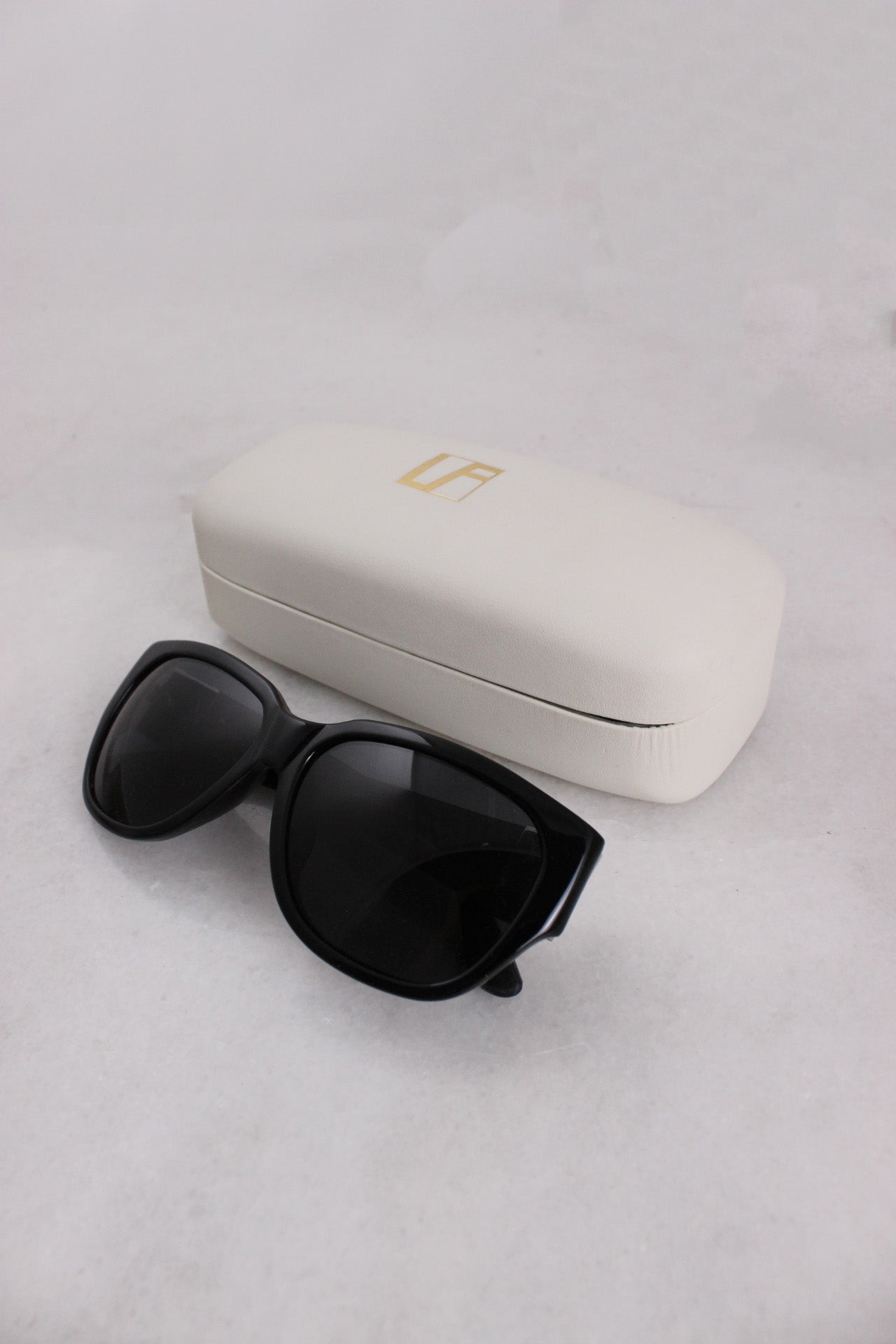 black sunglasses with branded case. case has text 'l f' on top. 
