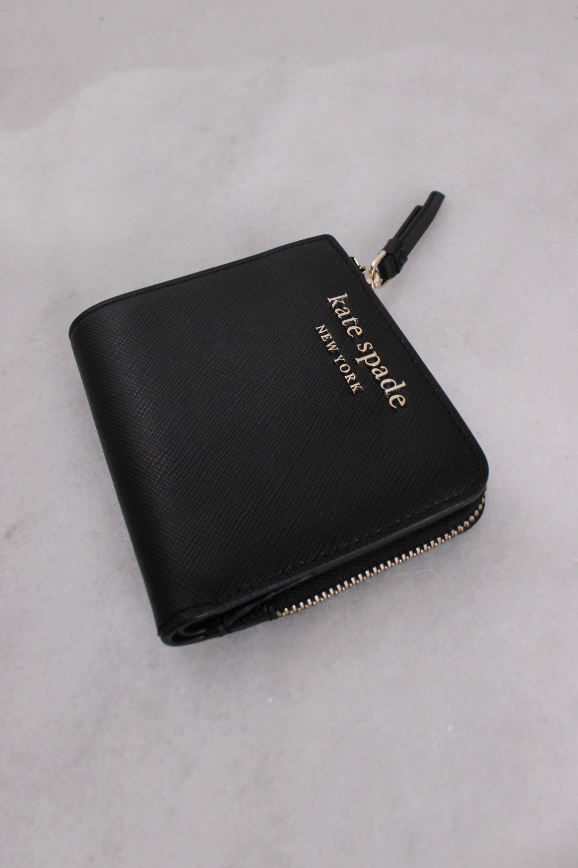 three-quarter front angle kate spade bifold wallet featuring 'kate spade' 'new york' gold-toned text and l-zip compartment.
