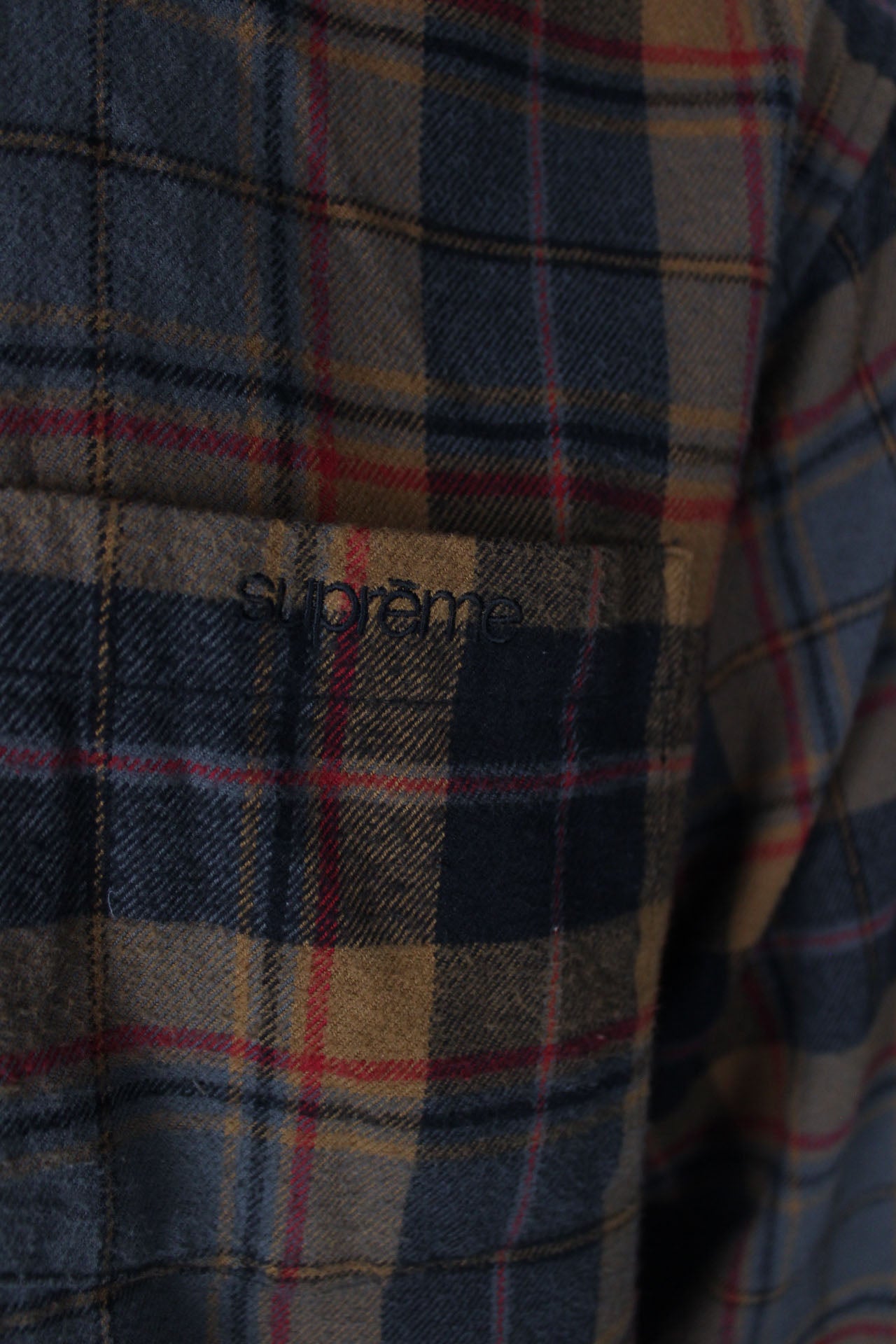 detail view with 'supreme' logo embroidered at left breast pocket of shirt.