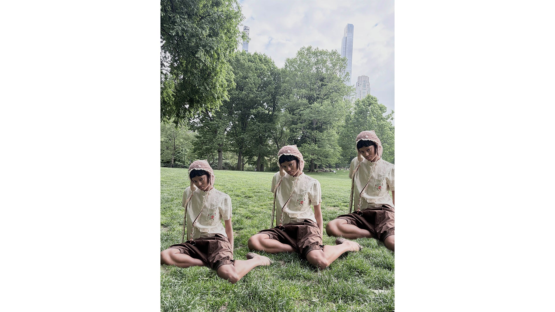Three people sitting on grass in a park with trees and a building in the background.