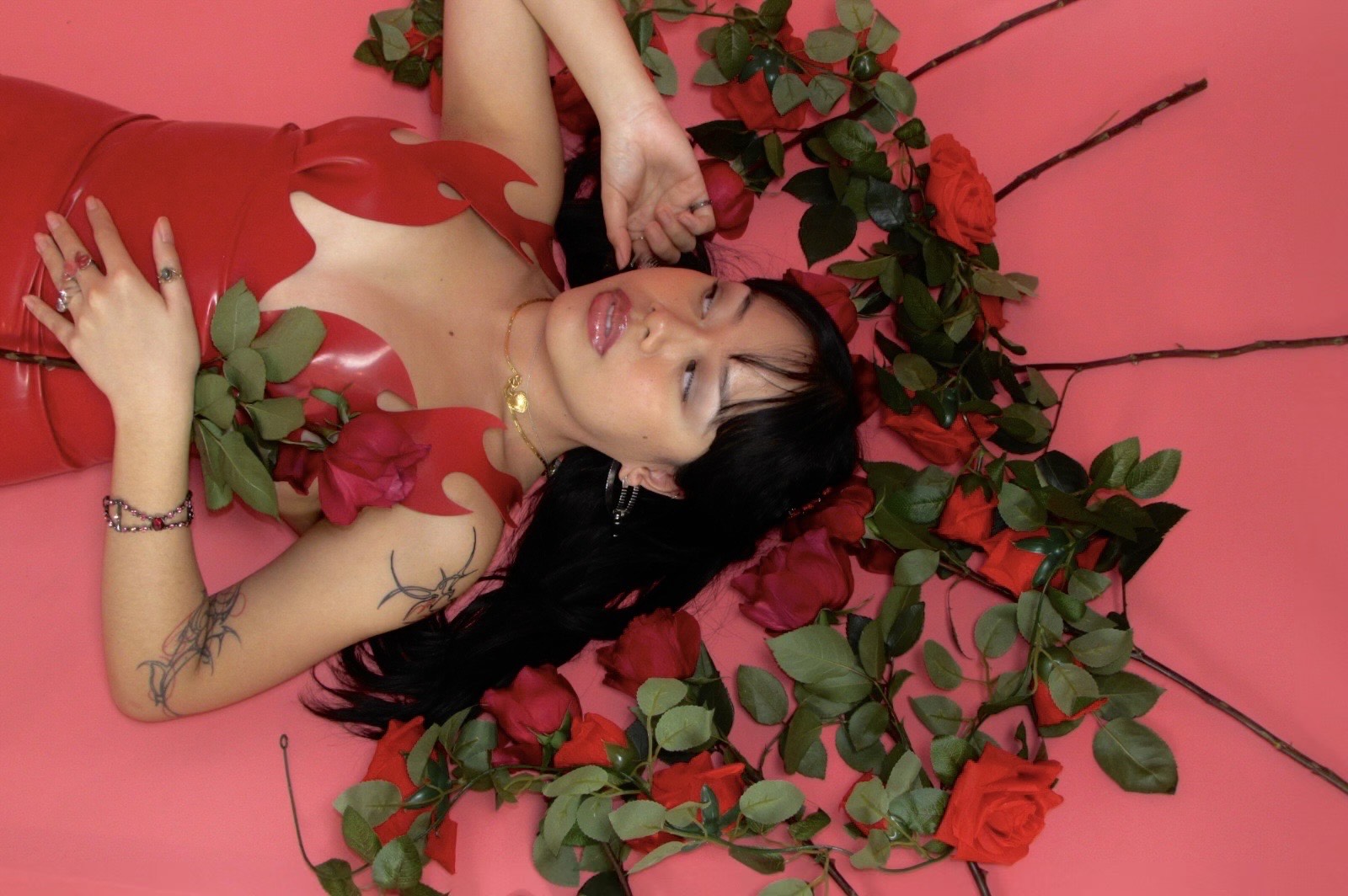 model in red latex dress lays with roses 