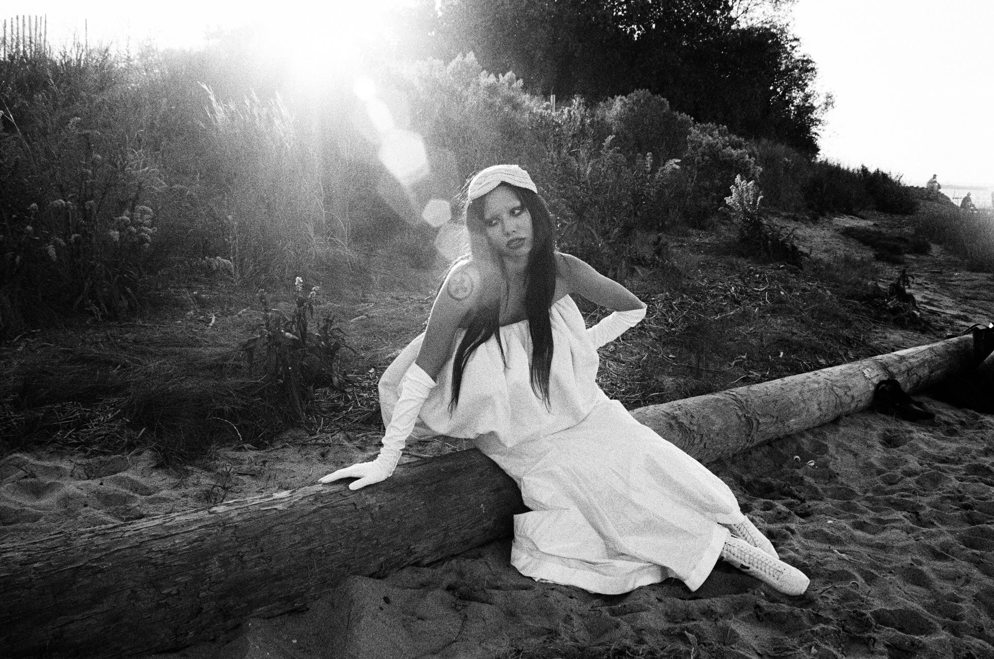 Person in a white dress sitting on a log on a beach
